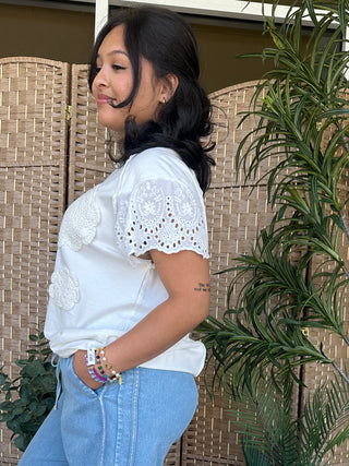 White crochet short-sleeve top with eyelet details and embroidered floral patterns on shoulders.
