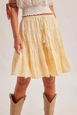Butter yellow tiered midi skirt with drawstring waist, paired with white smocked crop top and tan cowboy boots.
