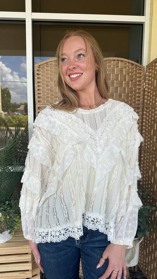 Cream lace ruffled blouse with textured fabric and lacy hem detail worn with dark jeans.
