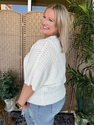 Cream knit asymmetrical sweater top with textured fabric and three-quarter sleeves.
