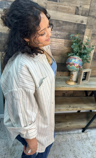 Ivory and black pinstriped button-down shirt with short sleeves worn over blue top.
