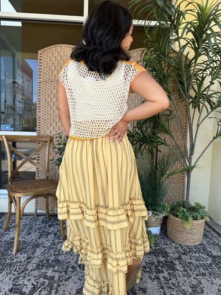 Cream open crochet sleeveless top with orange trim worn with yellow striped tiered ruffle skirt.

