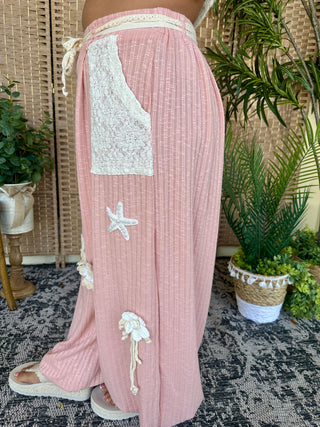 Blush pink ribbed joggers with white lace pocket detail and starfish appliqués.
