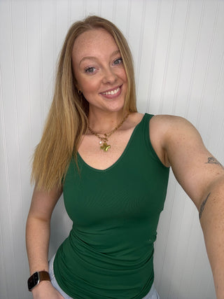 Dark green sleeveless tank top with ruched sides, v-neckline, worn with white pants.

