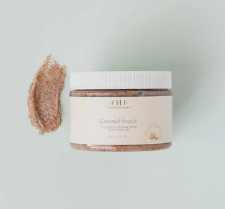 FHF Coconut Beach Sugar Scrub in a glass jar with lid, surrounded by tropical leaves and a fresh coconut.