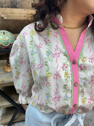 White cotton blouse with pink ribbons and yellow floral print, hot pink button-front trim, puffed sleeves.
