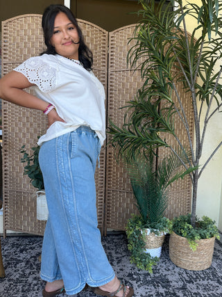 White crochet short-sleeve top with eyelet lace detail on shoulders, paired with blue denim jeans.
