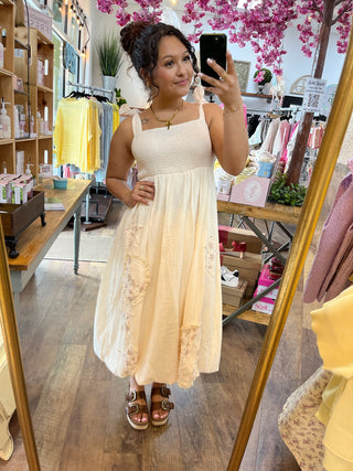 Cream textured midi dress with ruched bodice, adjustable straps, and floral embroidered side panels.
