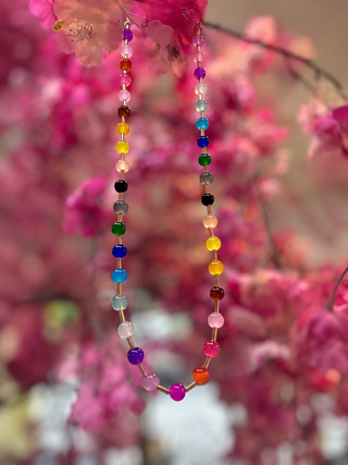 Multicolored glass bead necklace with rainbow beads strung on wire against pink floral background.
