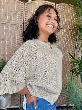 Taupe asymmetrical knit sweater top with openwork texture and draped sleeves.

