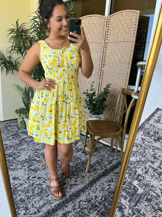 Yellow and white lemon print sleeveless mini dress with ruched waist and tiered skirt.
