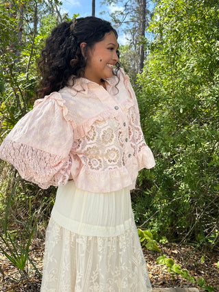 Blush pink lace shacket top with puffed sleeves and button front, worn with cream lace skirt.
