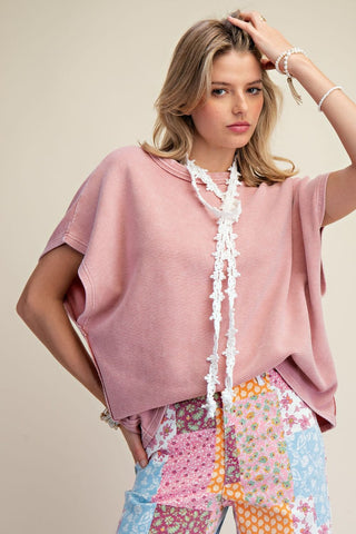 Dusty rose oversized drop shoulder tee with white lace trim detail, worn with colorful patchwork pants.
