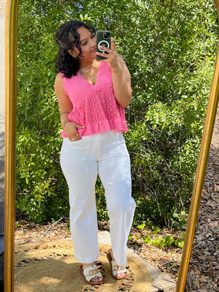 Bright pink textured V-neck sleeveless top with ruched detail paired with white pants.
