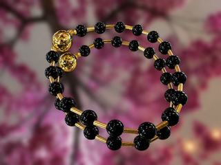 Black glass bead bracelet with gold accents and magnetic closures against floral background.
