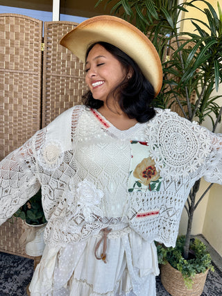 White crochet patchwork V-neck top with lace sleeves and floral detail worn by model.
