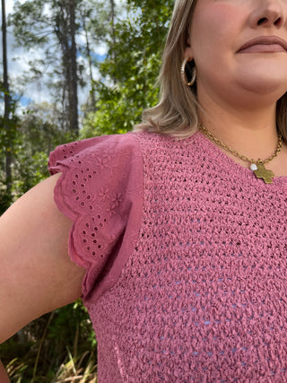 Mauve pink textured top with eyelet ruffle short sleeves and subtle crinkled fabric detail.
