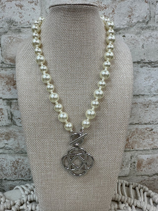 Cream pearl beaded necklace with silver clover charm pendant on display bust.
