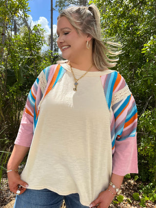 Ivory mineral wash top with colorful rainbow striped three-quarter sleeves and pink cuffs.
