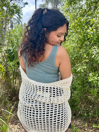 Cream crochet cardigan with open grid pattern over sage green ribbed tank top.
