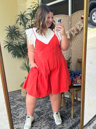 Red denim romper with adjustable straps and white short-sleeve shirt layered underneath.
