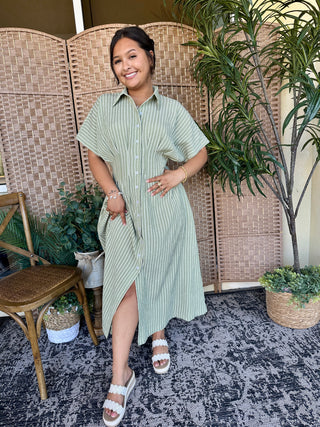 Sage green striped button-front shirt dress with short sleeves and side slit, styled casually.

