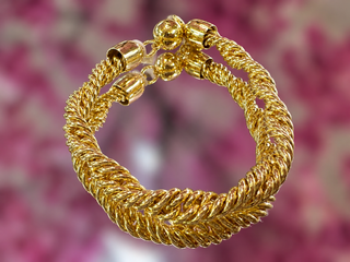 Gold braided twisted link bracelet with magnetic closure against blurred pink floral background.
