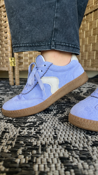 Lavender and cream suede sneaker with gum sole, lace-up style, worn with dark wash jeans.
