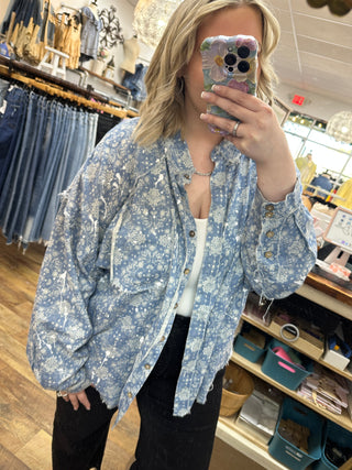 Blue and white paisley splatter print button-up long sleeve shirt worn as an open jacket over white tank top.
