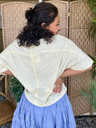 Cream textured short-sleeve top with center button closure, worn with periwinkle tiered skirt.
