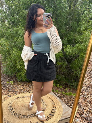 Black denim skort with drawstring waist paired with sage ribbed tank and cream crochet cardigan.
