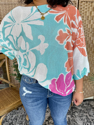 Multicolor floral batwing top with turquoise, coral, and pink blooms on white textured knit fabric.
