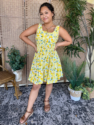 Yellow lemon print sleeveless mini dress with gathered skirt and front tie detail.
