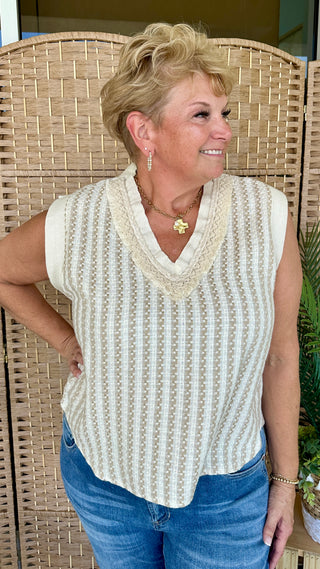 Cream and tan striped sleeveless knit top with v-neckline worn with blue jeans.
