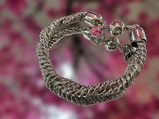 Silver braided twisted link bracelet with magnetic crystal ball closures against pink floral background.

