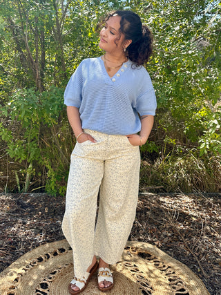 Sky blue textured short sleeve v-neck top with button detail, paired with cream floral pants.
