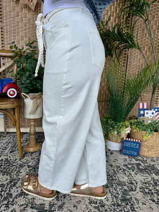 White gypsy fit pants with embroidered floral motifs and rope belt detail.
