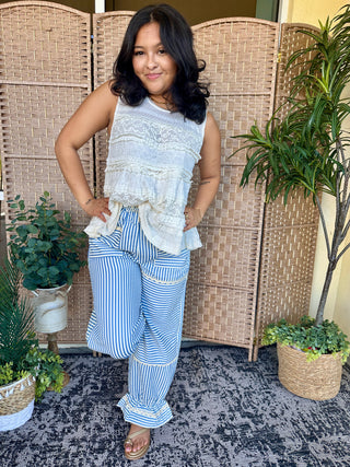 Ivory ruffle tank top with lace detailing paired with blue striped wide-leg pants.
