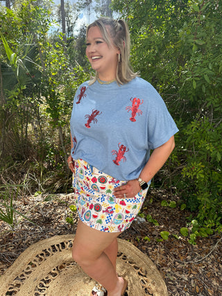 Light blue t-shirt with red sequin lobster print and colorful tropical pattern shorts.
