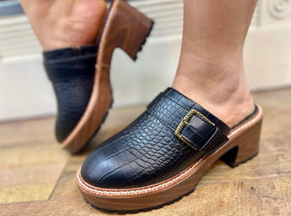 Black crocodile-embossed platform clog with buckle detail and tan sole.
