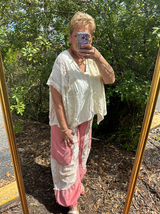 Ivory lace handkerchief top with asymmetrical hem and short sleeves worn with pink pants.
