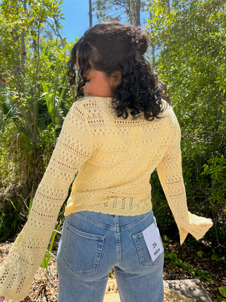 Cream yellow open-knit cardigan with long sleeves and scalloped edges worn over blue jeans.
