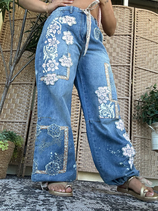 Blue denim jeans with white floral embroidery and patchwork details throughout.
