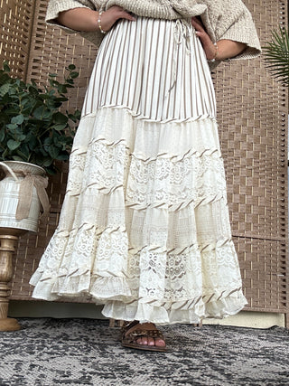 Cream pleated and lace tiered maxi skirt with ruffled layers and vertical striping detail.
