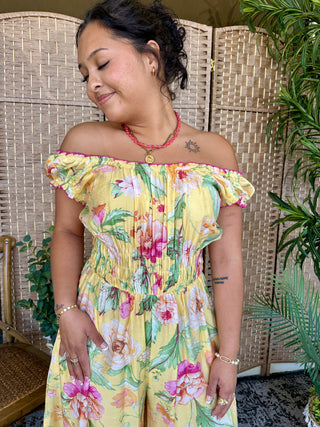 Yellow off-shoulder romper with colorful floral print and ruffled neckline.
