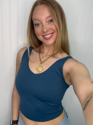 Teal blue seamless tank top with scoop neckline worn with gold chain necklace.
