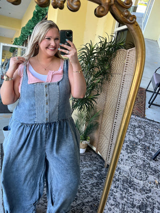 Oversized denim jumpsuit with pink collar and front pockets, light blue undershirt visible underneath.
