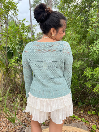 Sage green knit cardigan with open crochet pattern and long sleeves.

