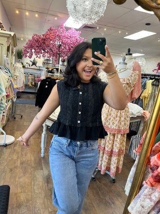 Black sleeveless button-up top with ruffle tiered hem and textured fabric.
