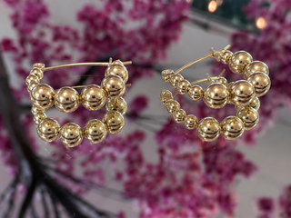 Gold bubble bead hoop earrings with layered spherical beads in varying sizes.
